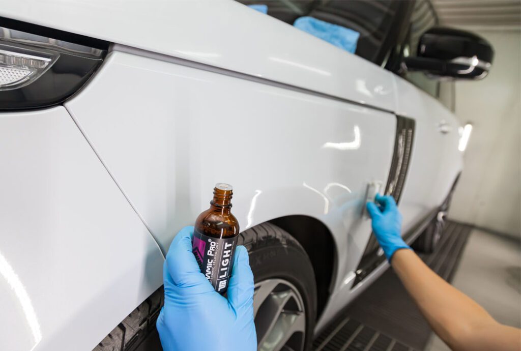 The process of applying a nano-ceramic coating Ceramic Pro 9h and Light on the car`s fender by a worker with a sponge and chemica